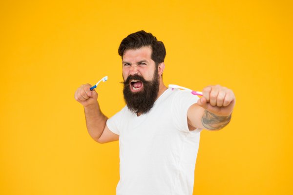Man with a toothbrush in both hands against a yellow background